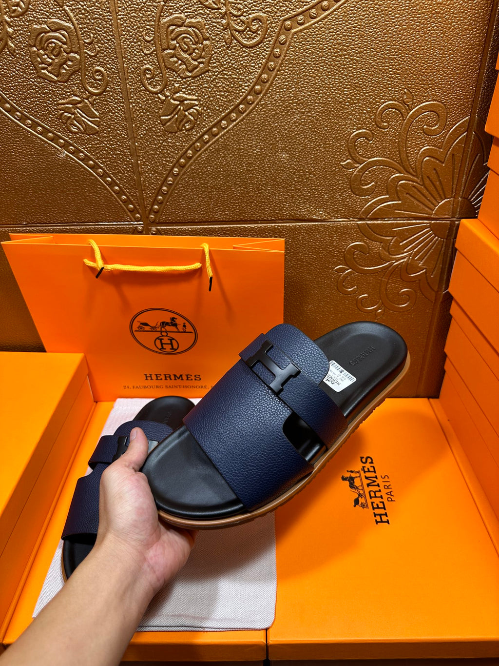 Hermes dark blue slide sandals held by hand, with wide buckle straps