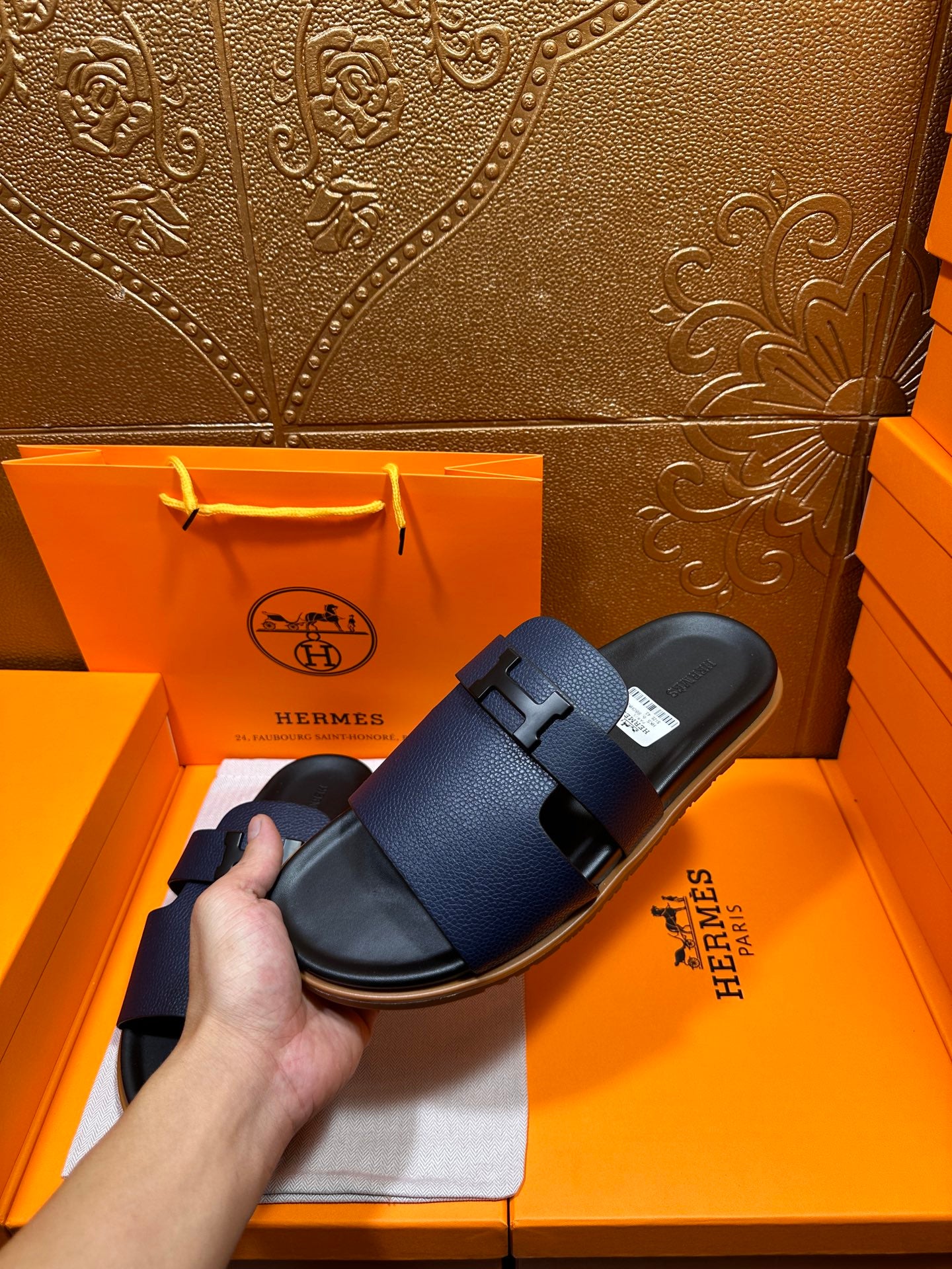 Hermes dark blue slide sandals held by hand, with wide buckle straps