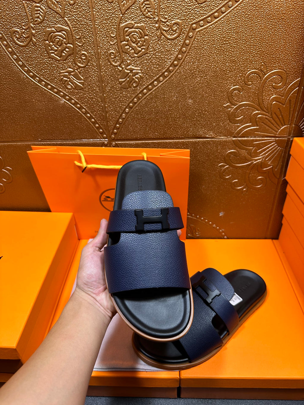 Hermes dark blue slide sandal held up, showing single front strap and buckle