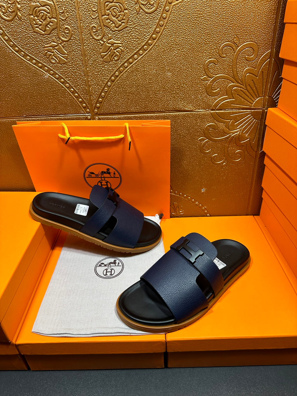 Hermes dark blue slide sandals with wide buckle straps, stacked on tray
