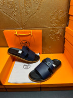 Hermes dark blue slide sandals with wide buckle straps, stacked on tray