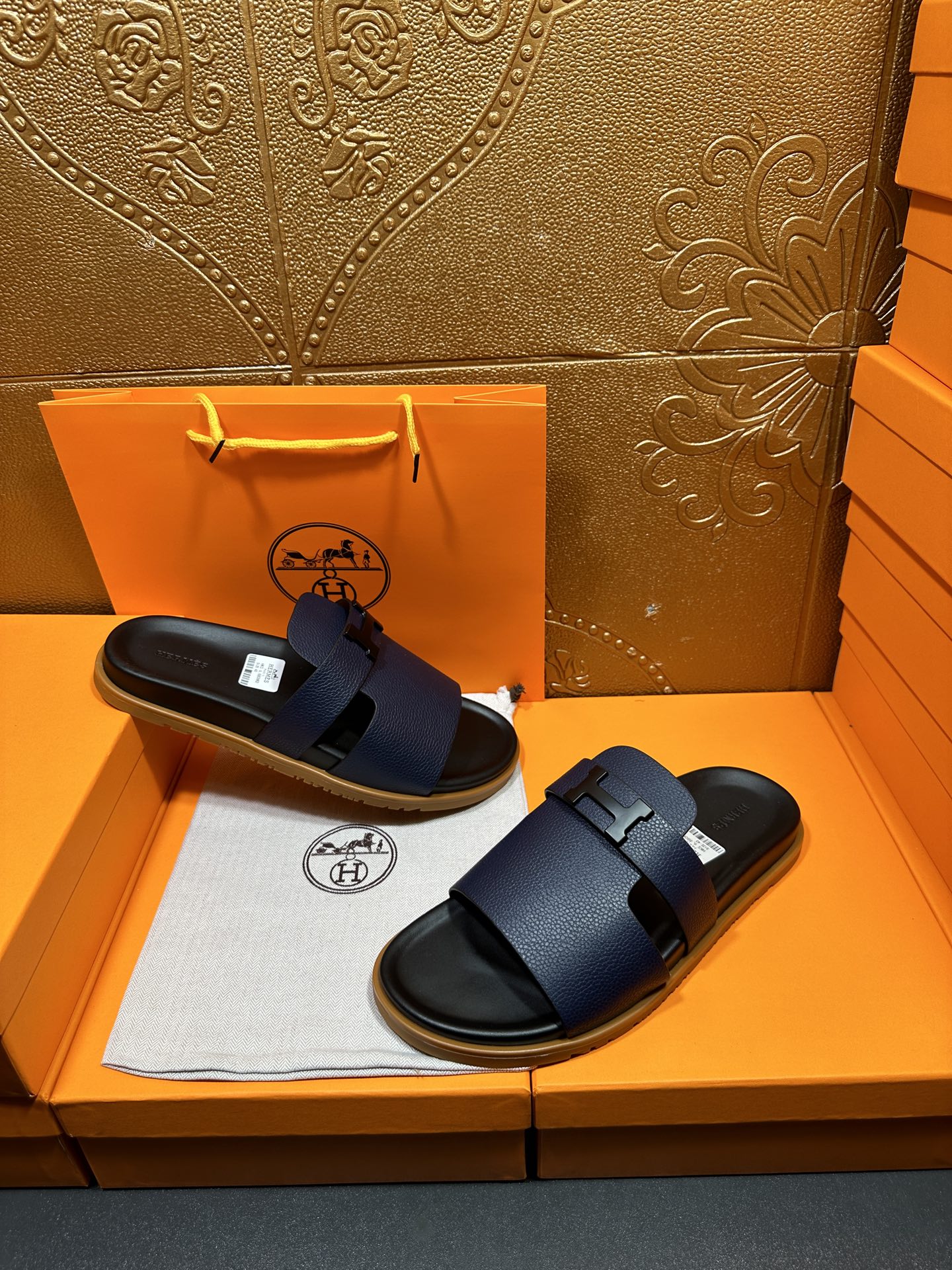 Hermes dark blue slide sandals with wide buckle straps, stacked on tray