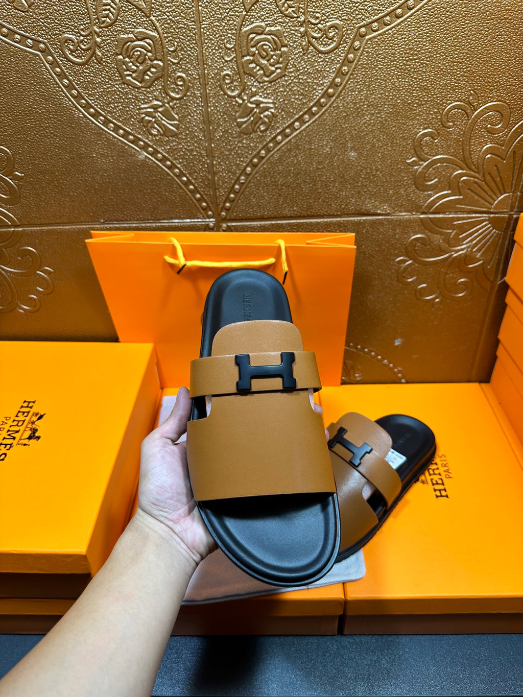 Hermes tan slide sandals with black H buckle, blue lining visible at the footbed
