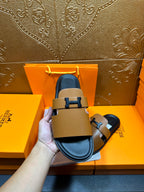 Hermes tan slide sandals with black H buckle, blue lining visible at the footbed