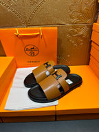 Hermes slide sandals featuring tan leather straps and a black H buckle on black sole