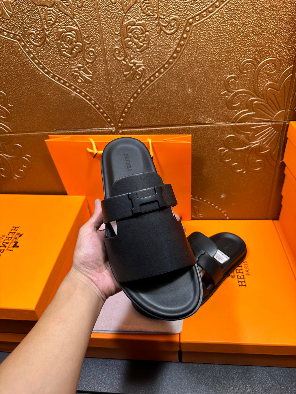 Black leather slide sandals held in hand, side profile with adjustable buckle strap