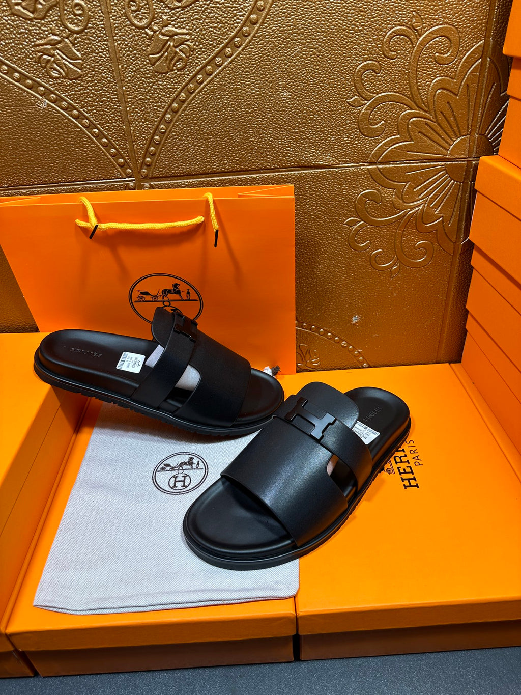 Black leather slide sandals with wide straps and adjustable buckle, pair laid out