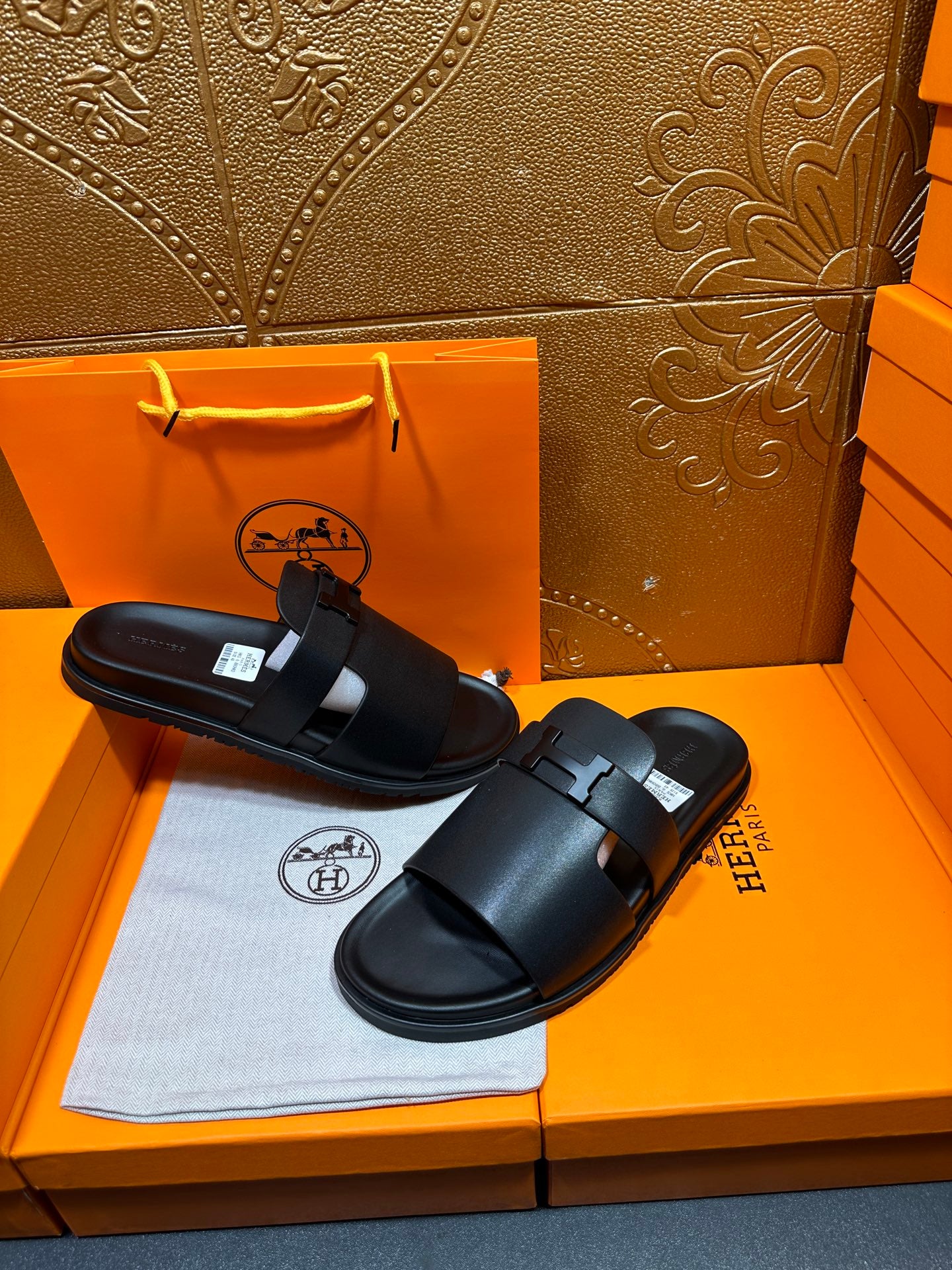 Black leather slide sandals with wide straps and adjustable buckle, pair laid out