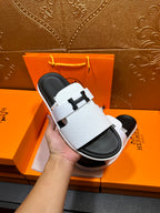 Hermes slide sandals, white straps with H buckle, held in hand