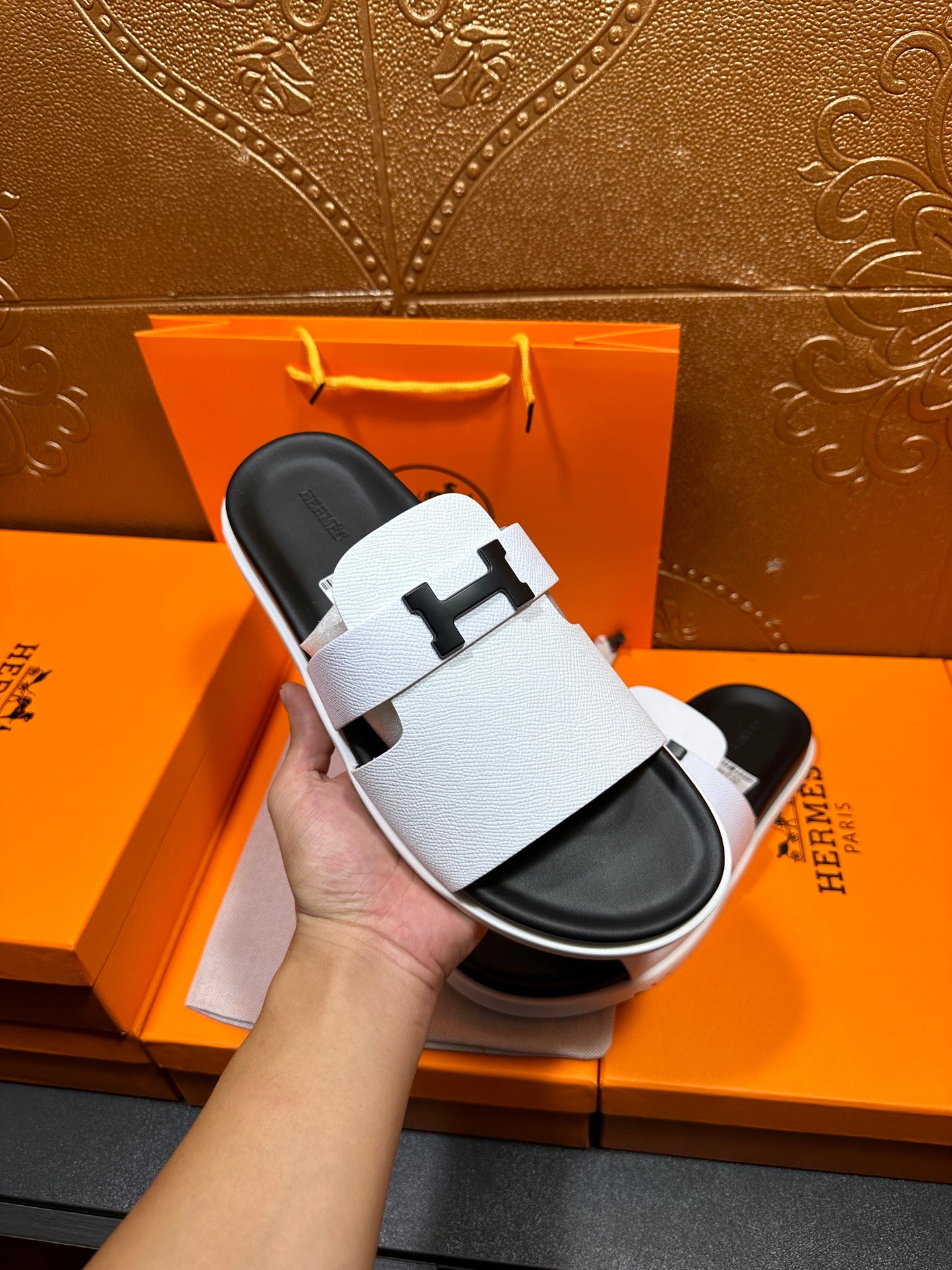 Hermes slide sandals, white straps with H buckle, held in hand