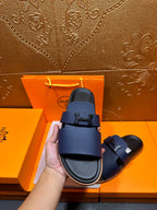 Dark blue leather slide sandal with buckle strap shown on black footbed