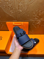 Hand holding dark blue leather slide sandals with black base and buckle strap