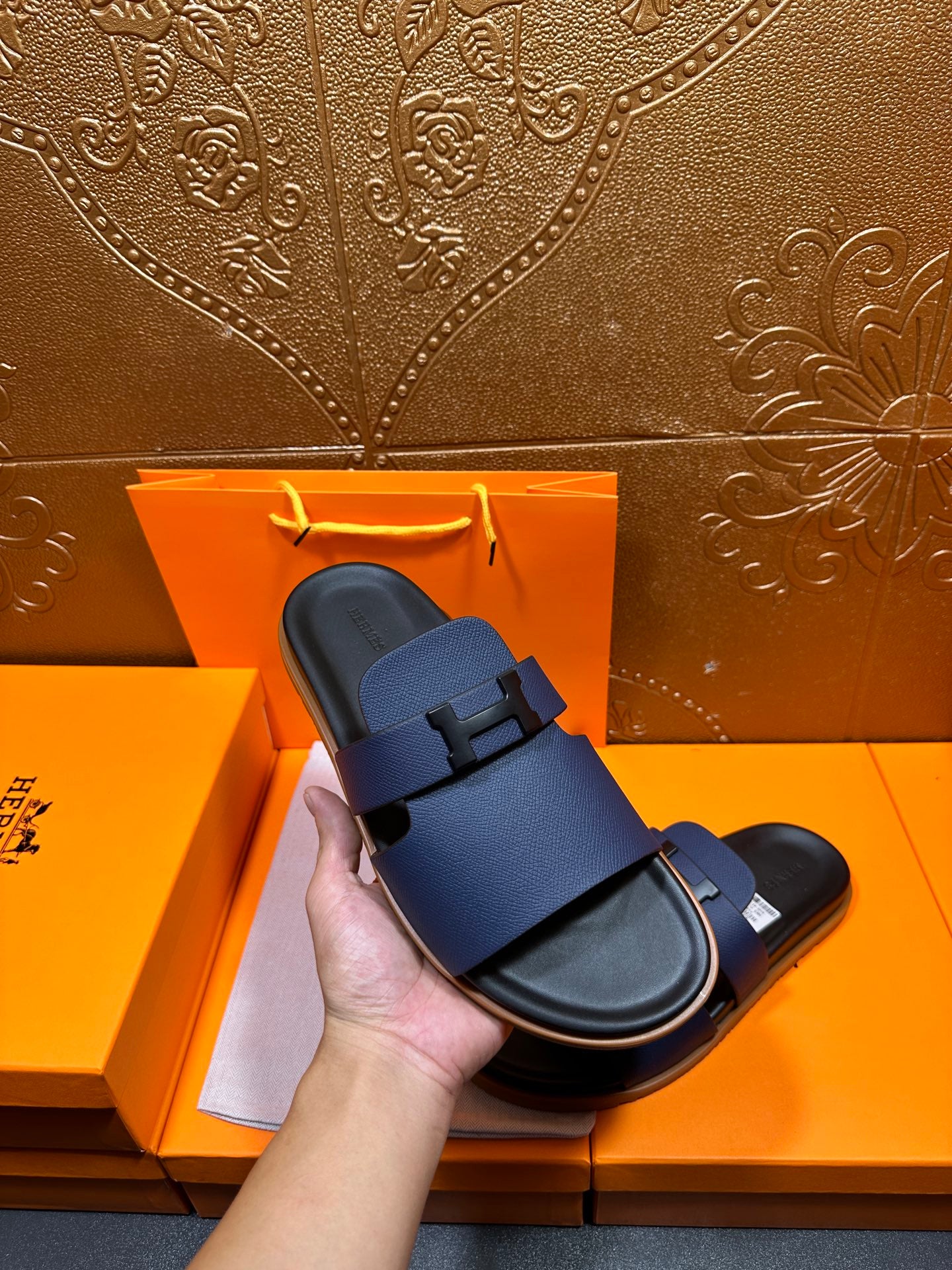 Hand holding dark blue leather slide sandals with black base and buckle strap