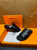 Black leather slide sandals with double strap design and wide buckle closure.