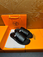 Black leather slide sandals with curved footbed and front buckle strap detail.