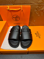 Black leather slide sandals, two wide straps with buckle closures.