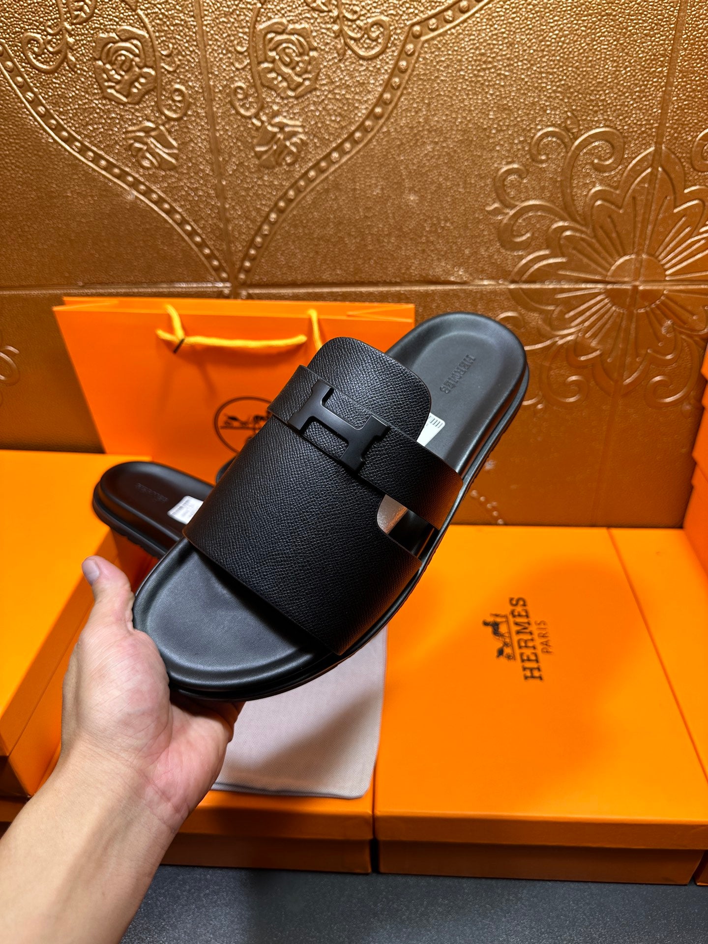 Black leather slide sandal held in hand, rounded toe and wide buckle strap.