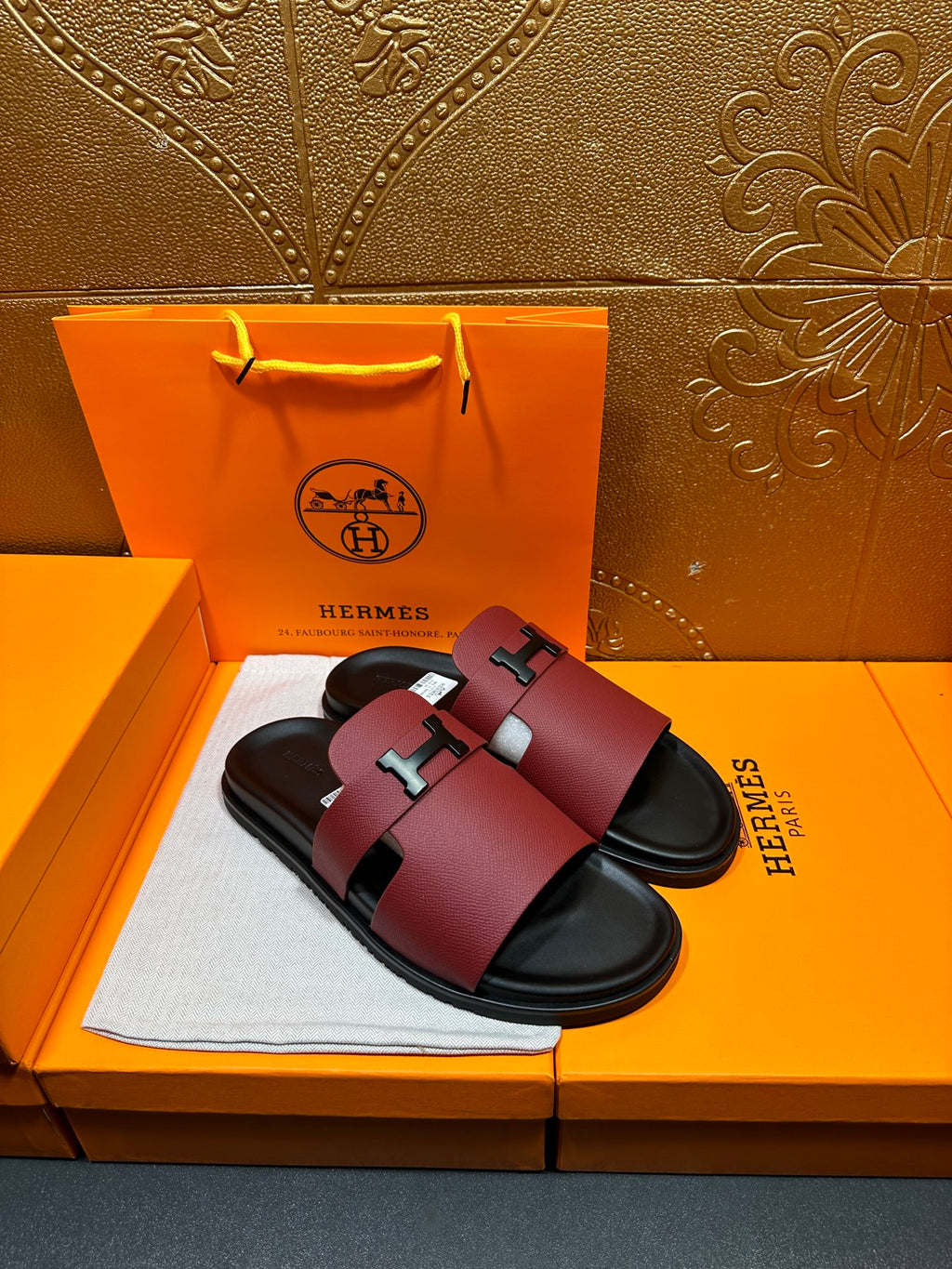 Hermes slide sandals, burgundy leather with silver H buckle and black rubber footbed.