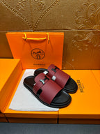 Hermes slide sandals, burgundy leather with silver H buckle and black rubber footbed.