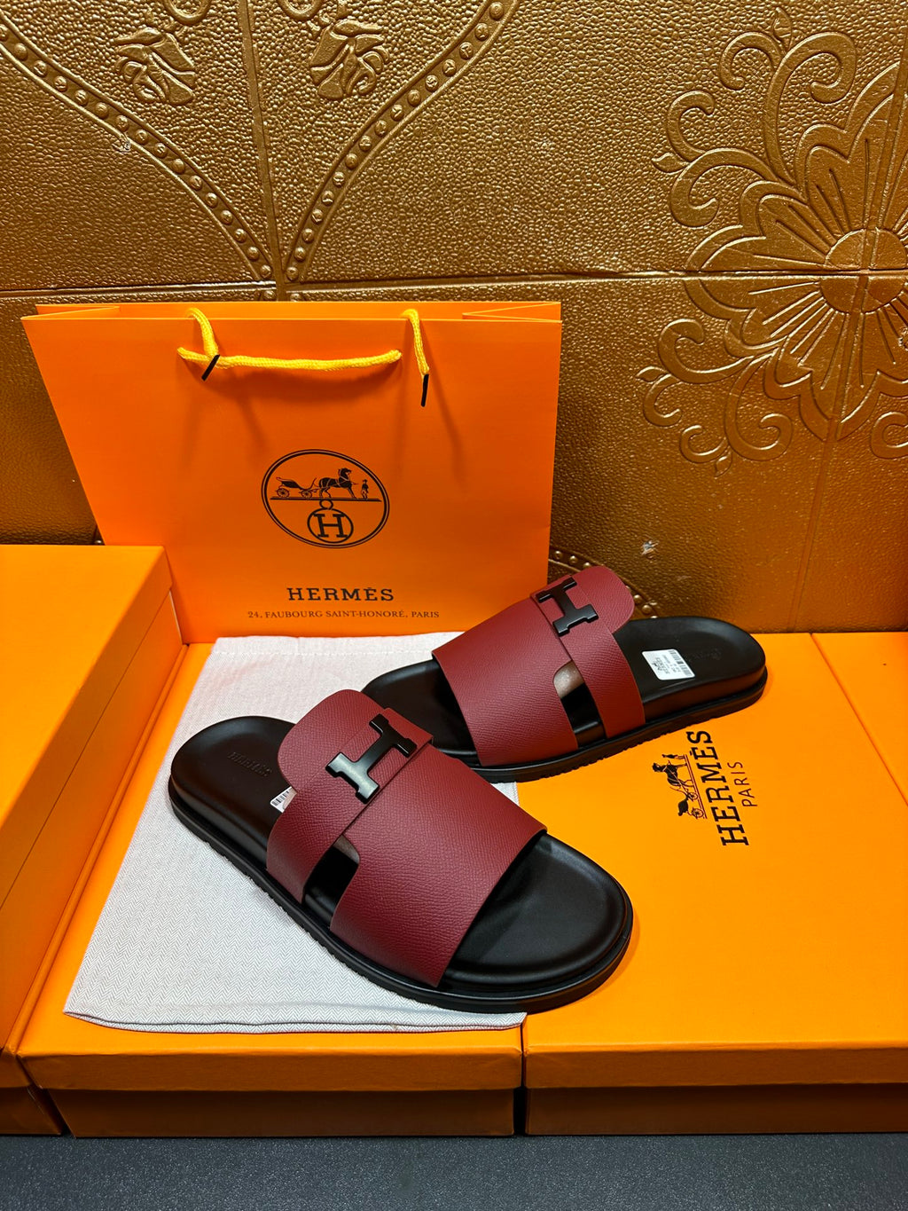 Hermes slide sandals in burgundy leather with silver H buckle across black footbed.
