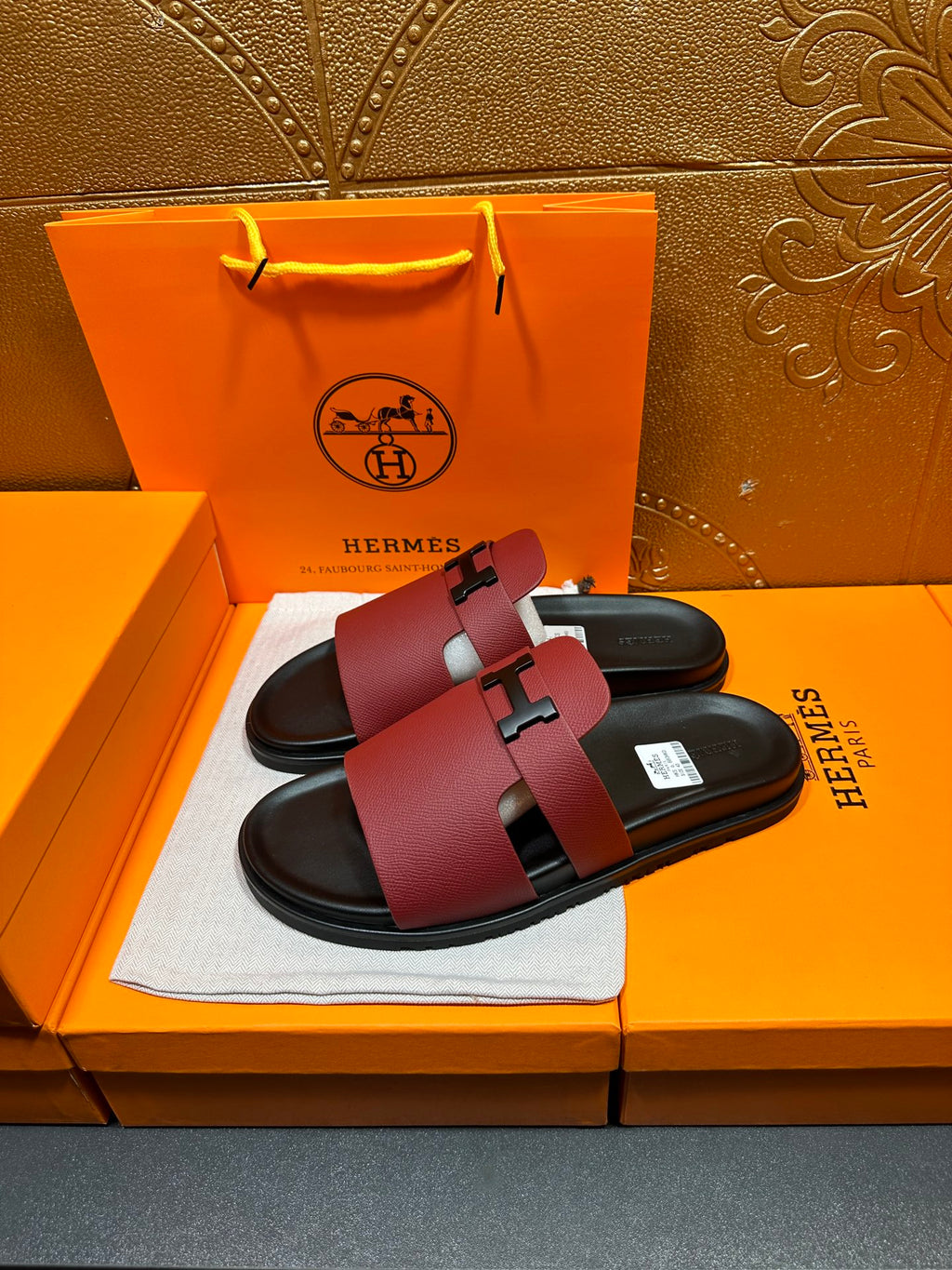 Hermes slide sandals with burgundy straps and silver H buckle over black sandals soles.