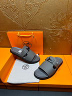 Dark gray slide sandals placed side by side, square H buckle on thick straps
