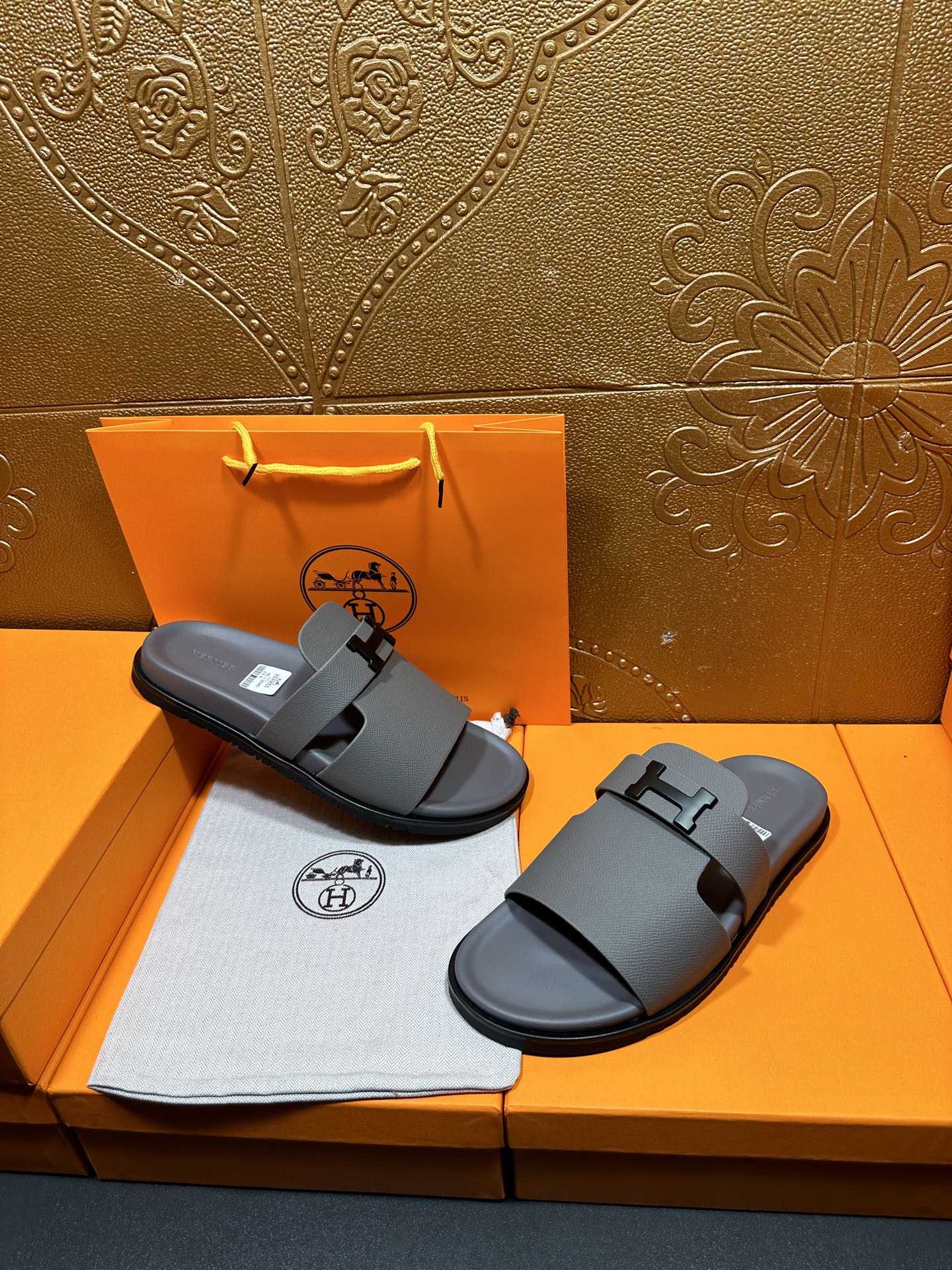 Dark gray slide sandals placed side by side, square H buckle on thick straps