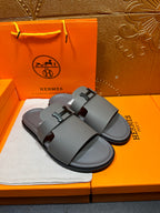 Dark gray slide sandals with square H buckle and textured footbed, pair view