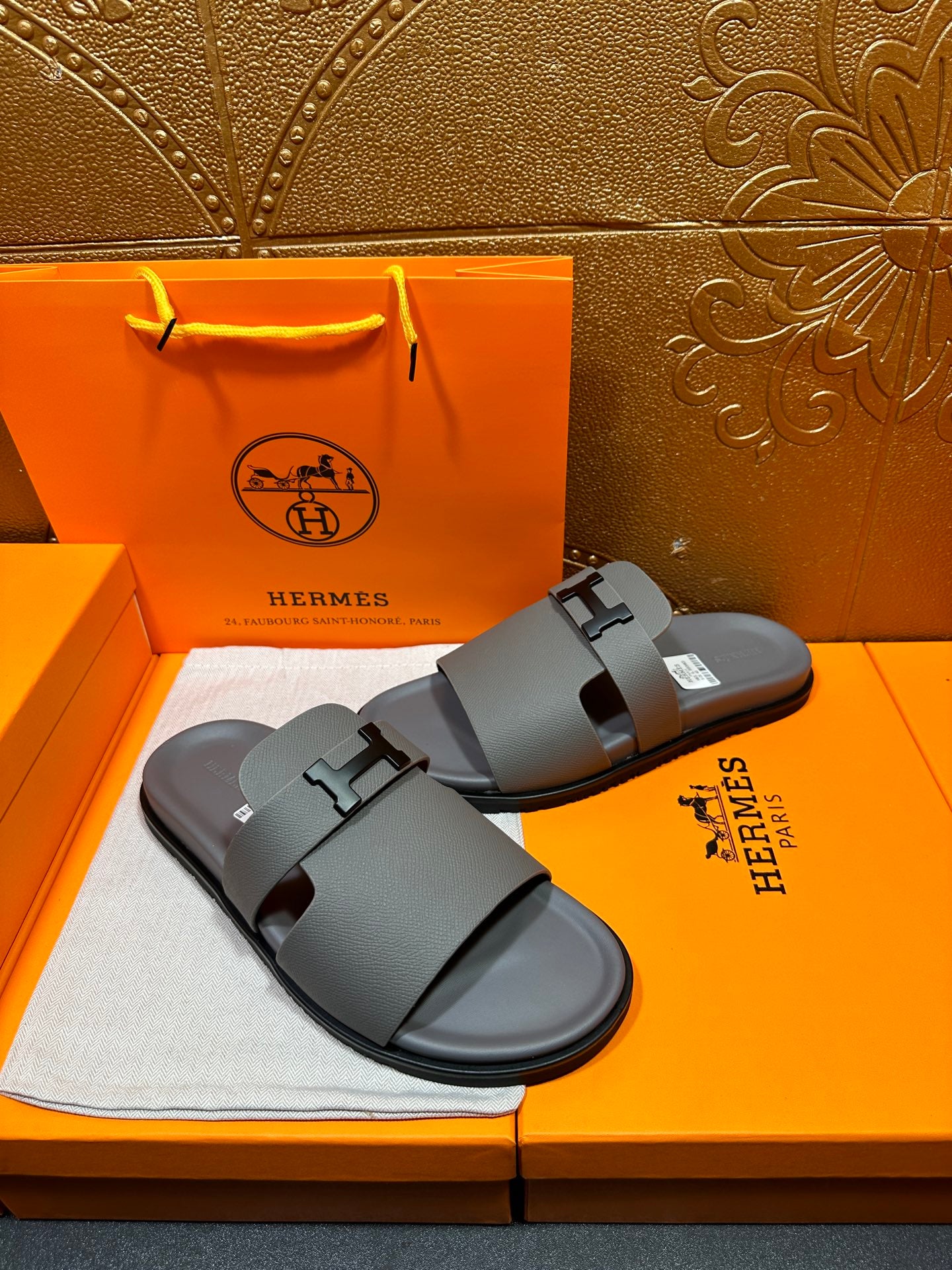 Dark gray slide sandals with square H buckle and thick straps, angled side view