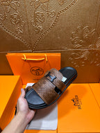 Hermes sandals held in hand with brown textured straps and black footbed, metal buckle