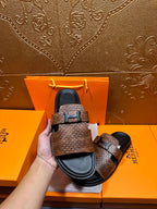 Hermes sandals held in hand: brown textured upper, black sole, metal H-style buckle