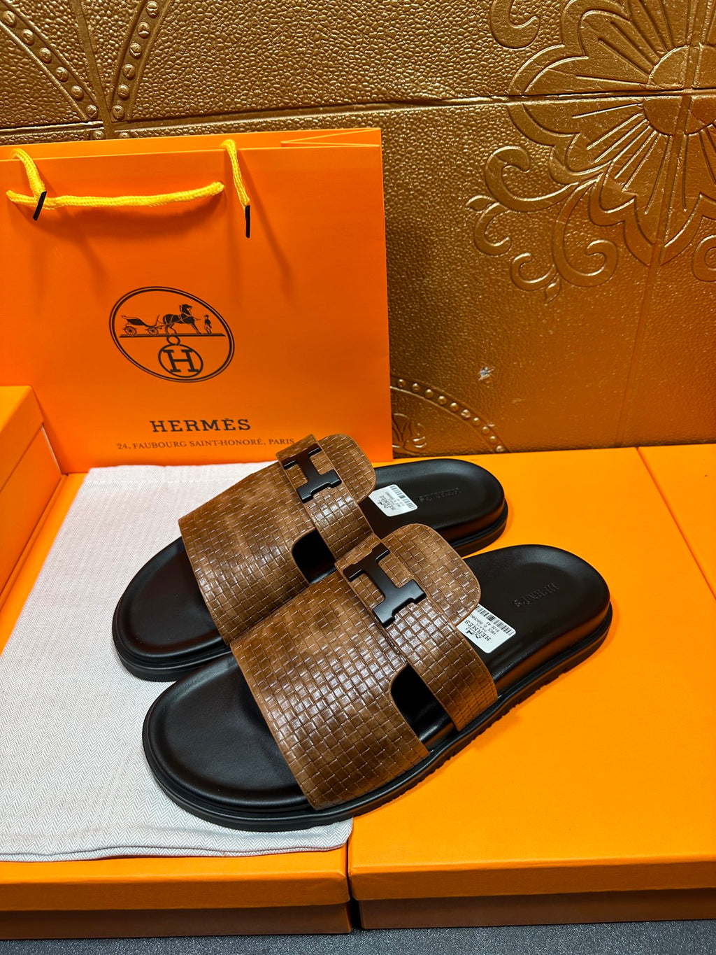 Hermes slide sandals with brown textured straps and black soles, metal buckle detail