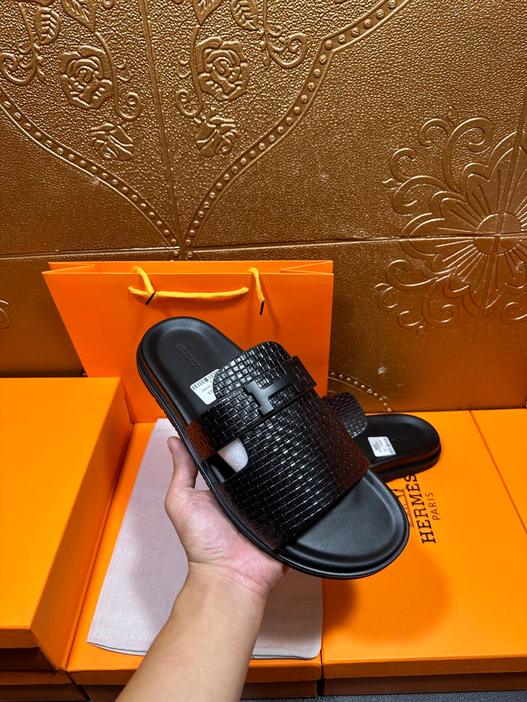 Hermes black textured slide sandal held in hand, wide strap over black footbed