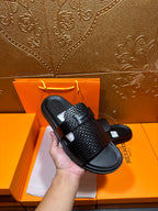 Hermes black textured slide sandal held in hand, wide strap over black footbed