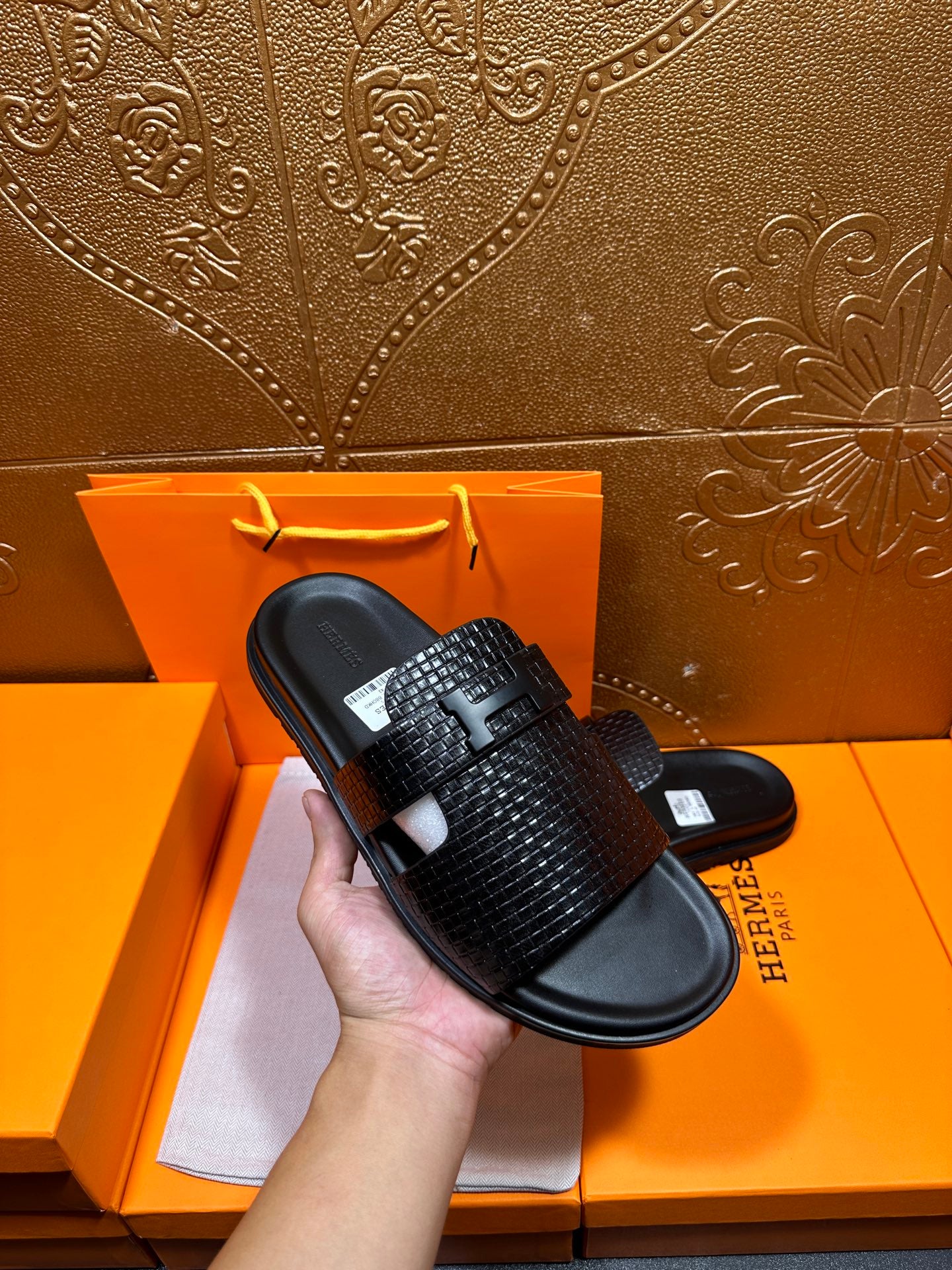 Hermes black textured slide sandal held in hand, wide strap over black footbed