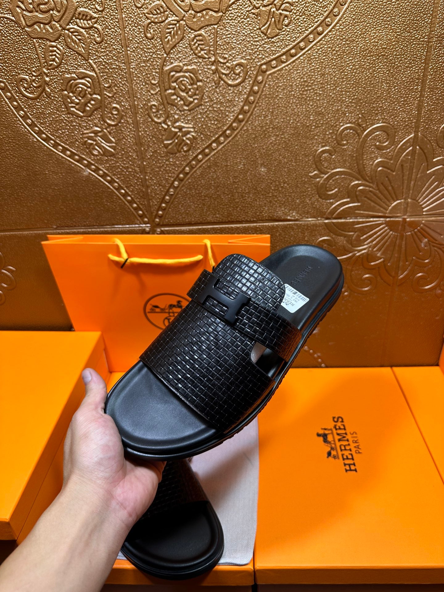 Hermes black textured slide sandals, one held above the other on cushioned footbeds