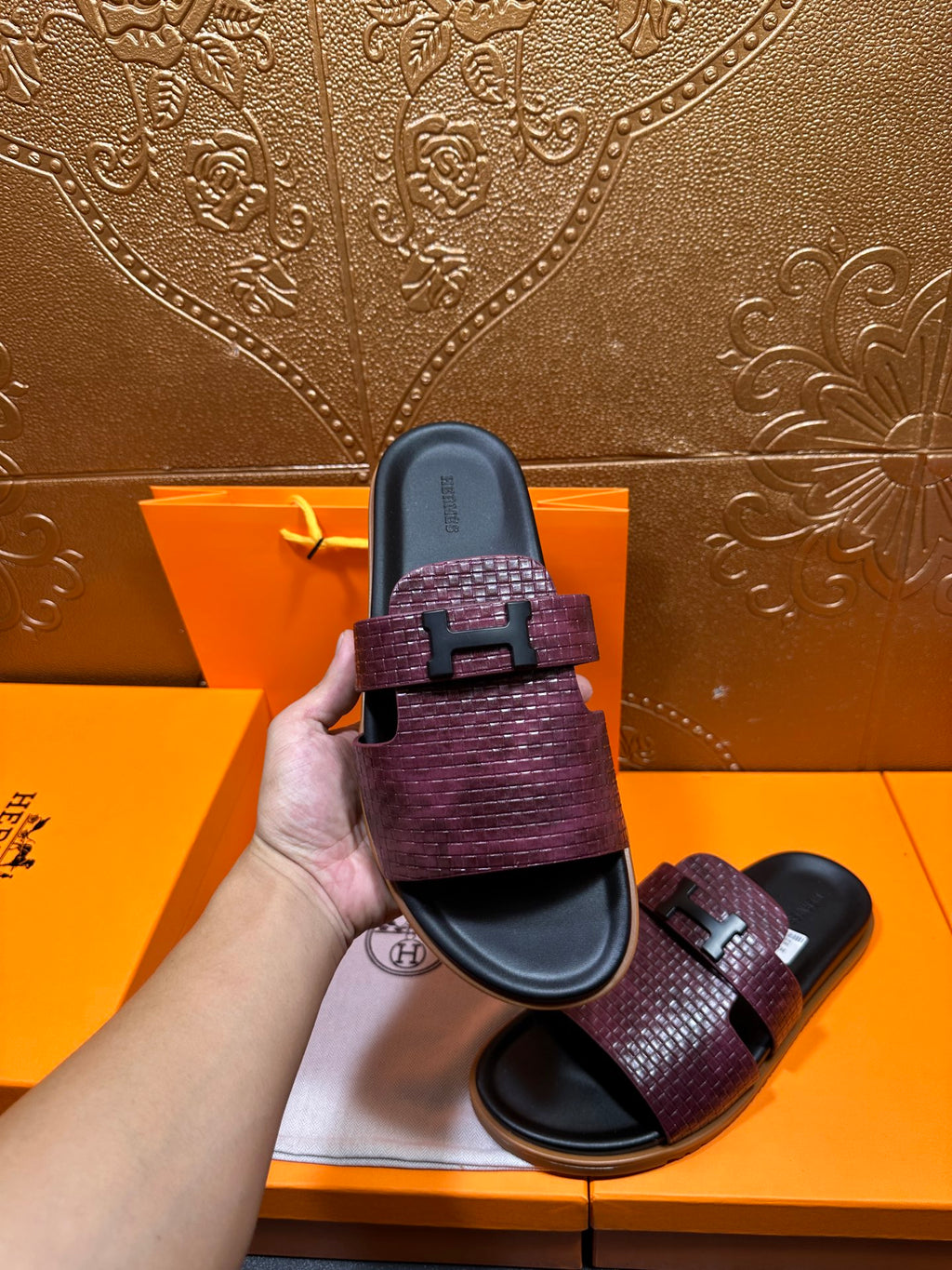 Hermes slide sandal held up, burgundy textured strap with black buckle and dark footbed