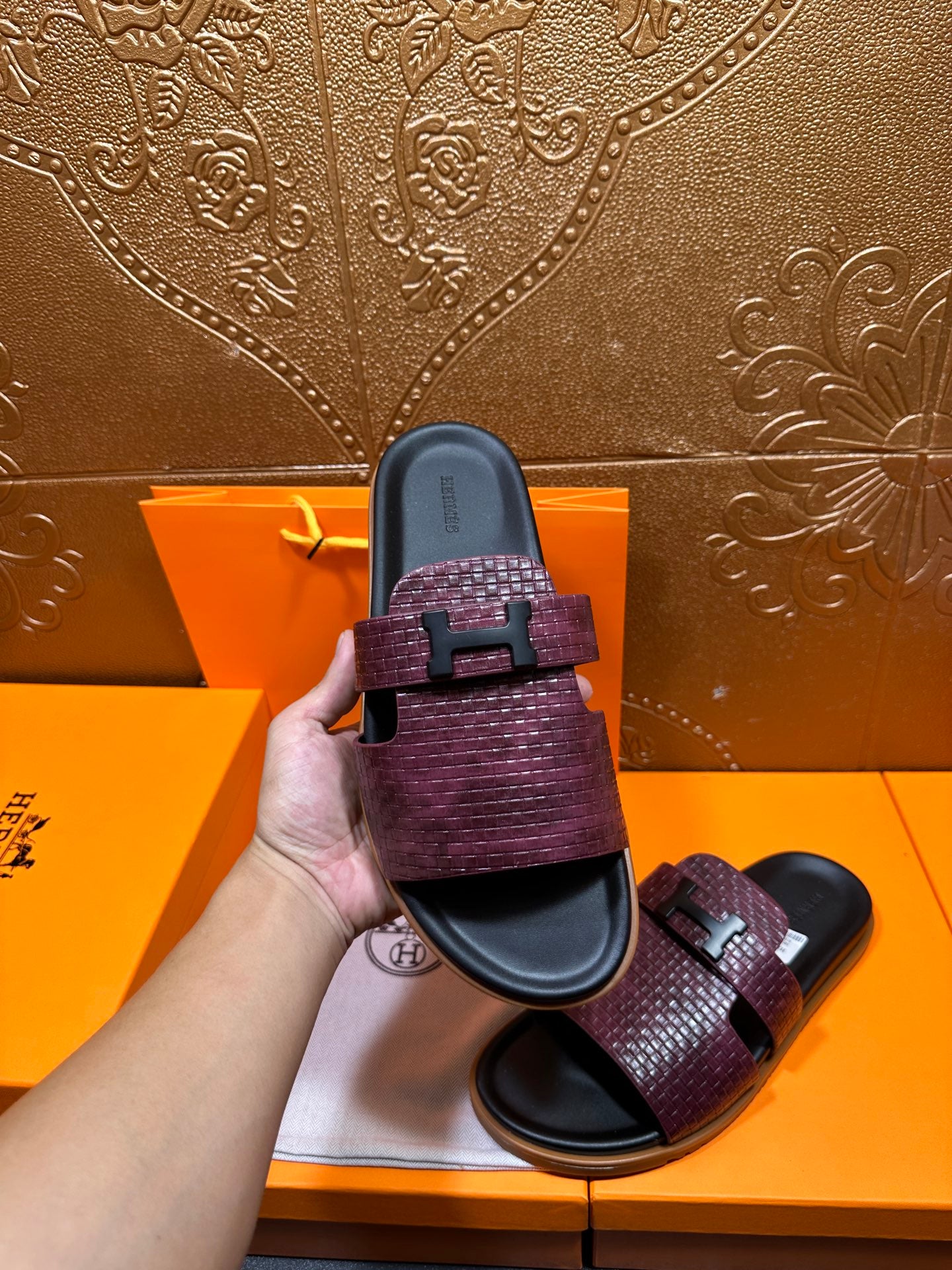 Hermes slide sandal held up, burgundy textured strap with black buckle and dark footbed