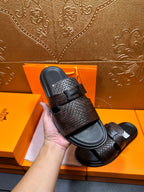Hermes textured slide sandal held up, dark brown woven strap and black footbed