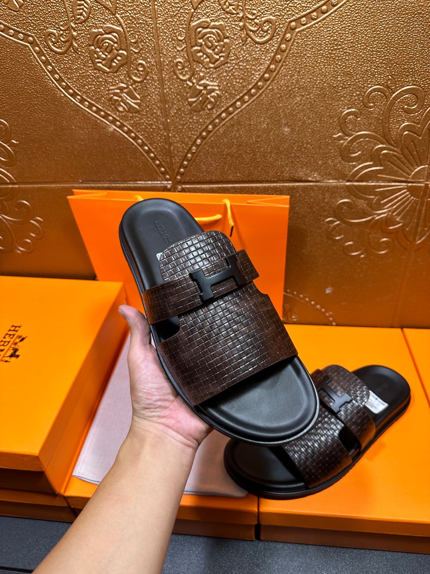 Hermes textured slide sandal held up, dark brown woven strap and black footbed