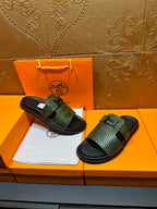 Hermes slide sandals with green textured straps and black rubber soles, displayed pair