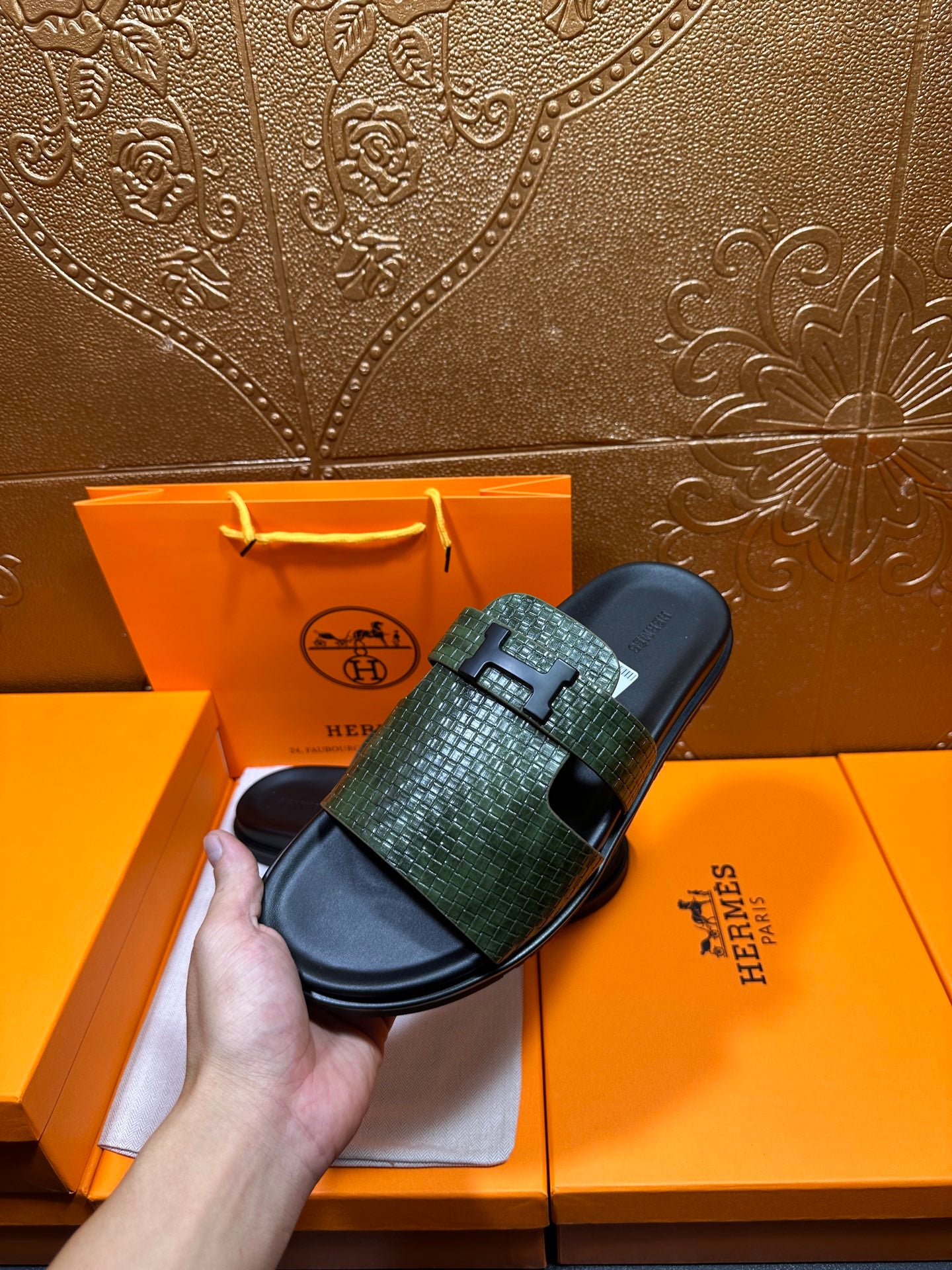 Hermes slide sandals with green textured straps and black soles, one shoe held up