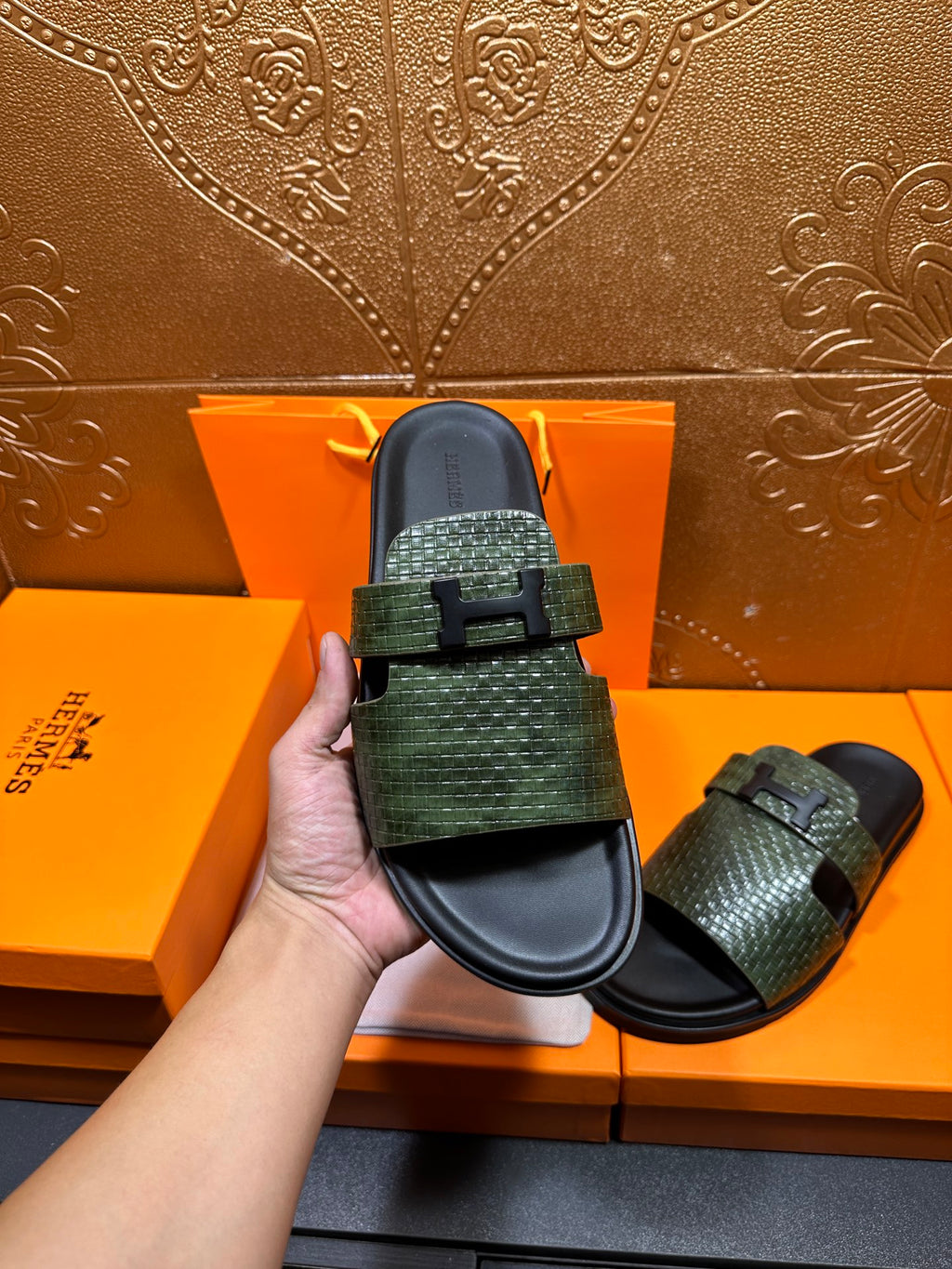 Hermes slide sandals with green textured upper straps and black footbed, one held