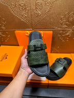 Hermes slide sandals with green textured upper straps and black footbed, one held