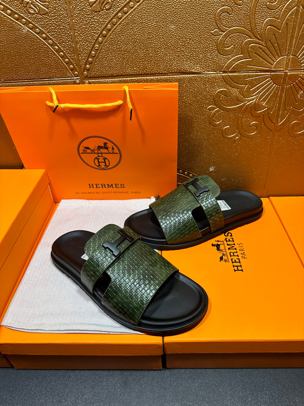 Hermes slide sandals with green textured straps and black soles, angled pair
