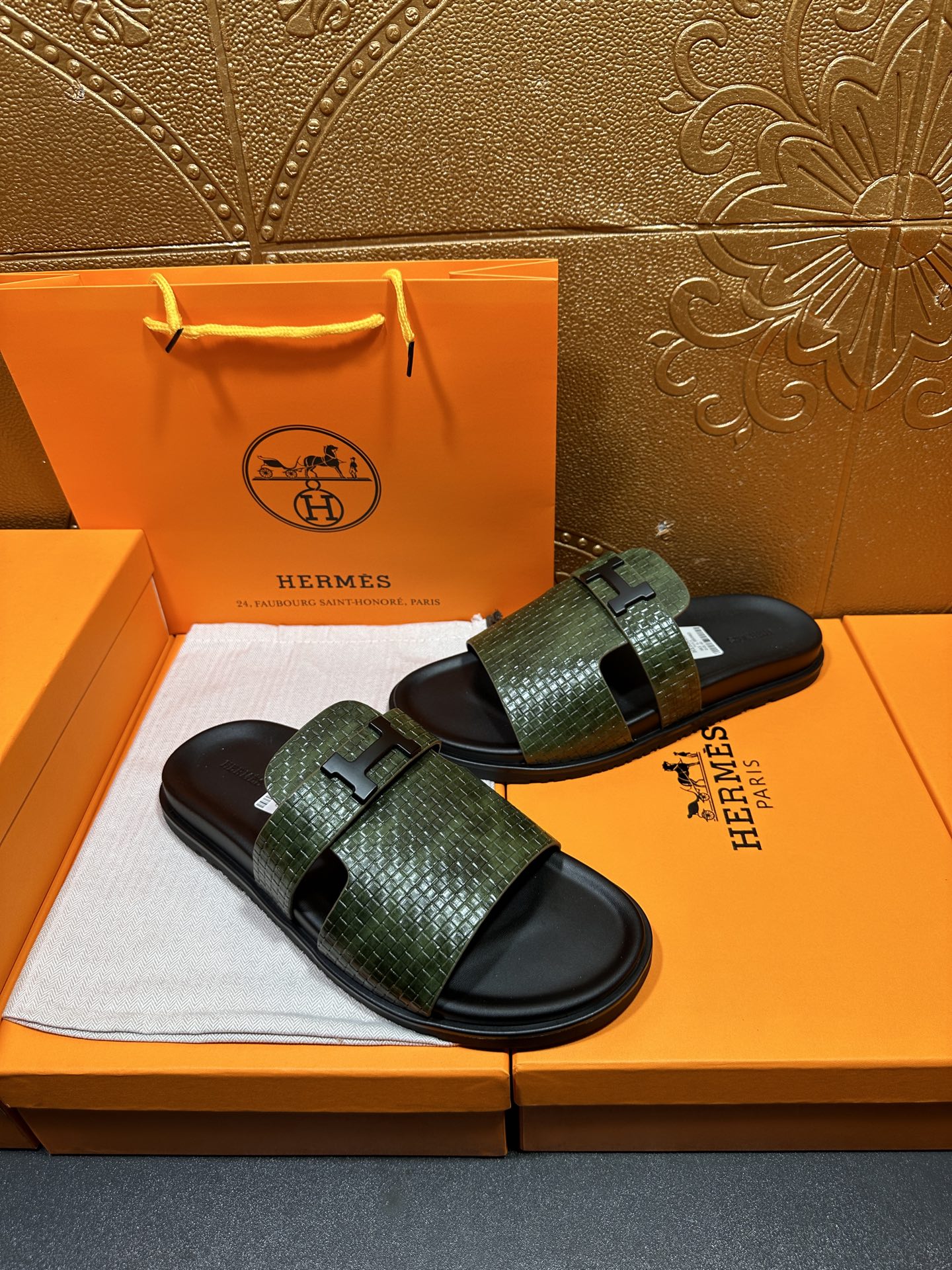 Hermes slide sandals with green textured straps and black soles, angled pair