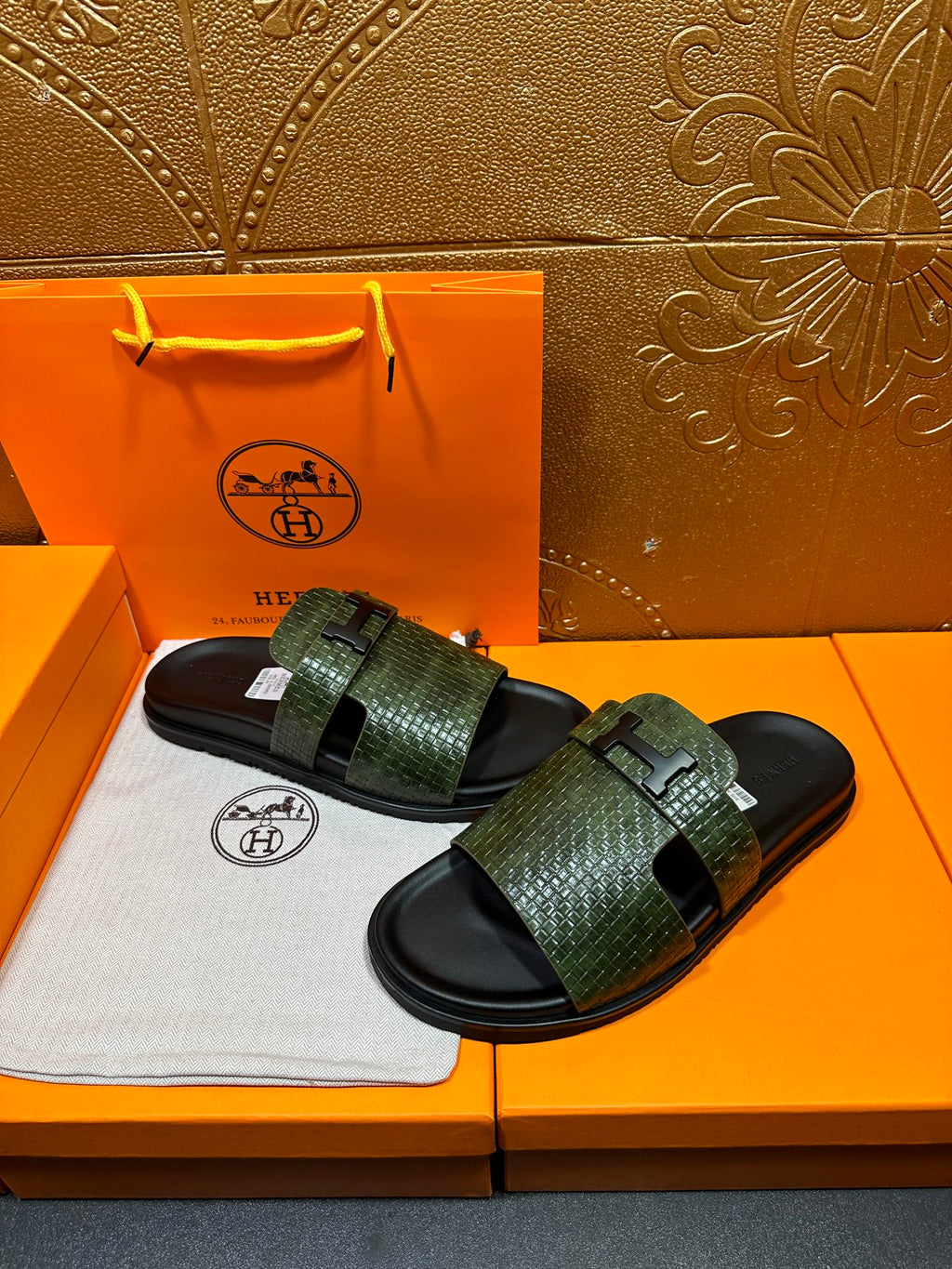 Hermes slide sandals with green patterned straps and black rubber footbeds, worn in pair