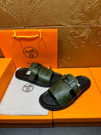 Hermes slide sandals with green patterned straps and black rubber footbeds, worn in pair