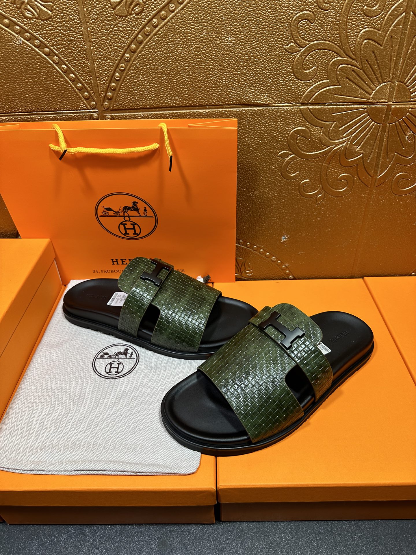 Hermes slide sandals with green patterned straps and black rubber footbeds, worn in pair