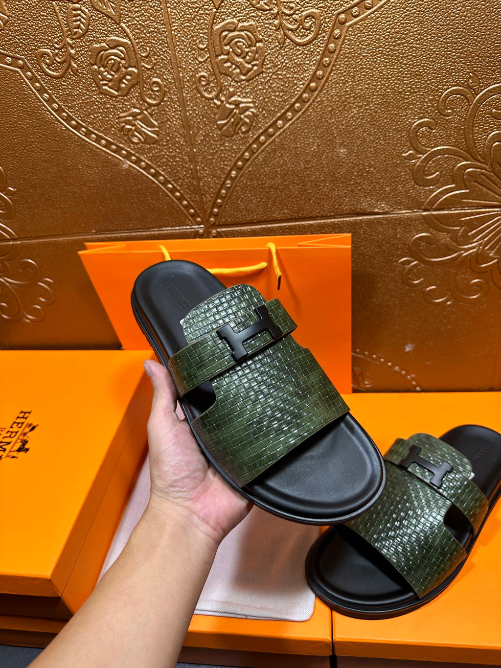 Hermes slide sandals with green textured straps and black footbeds, hand holding one